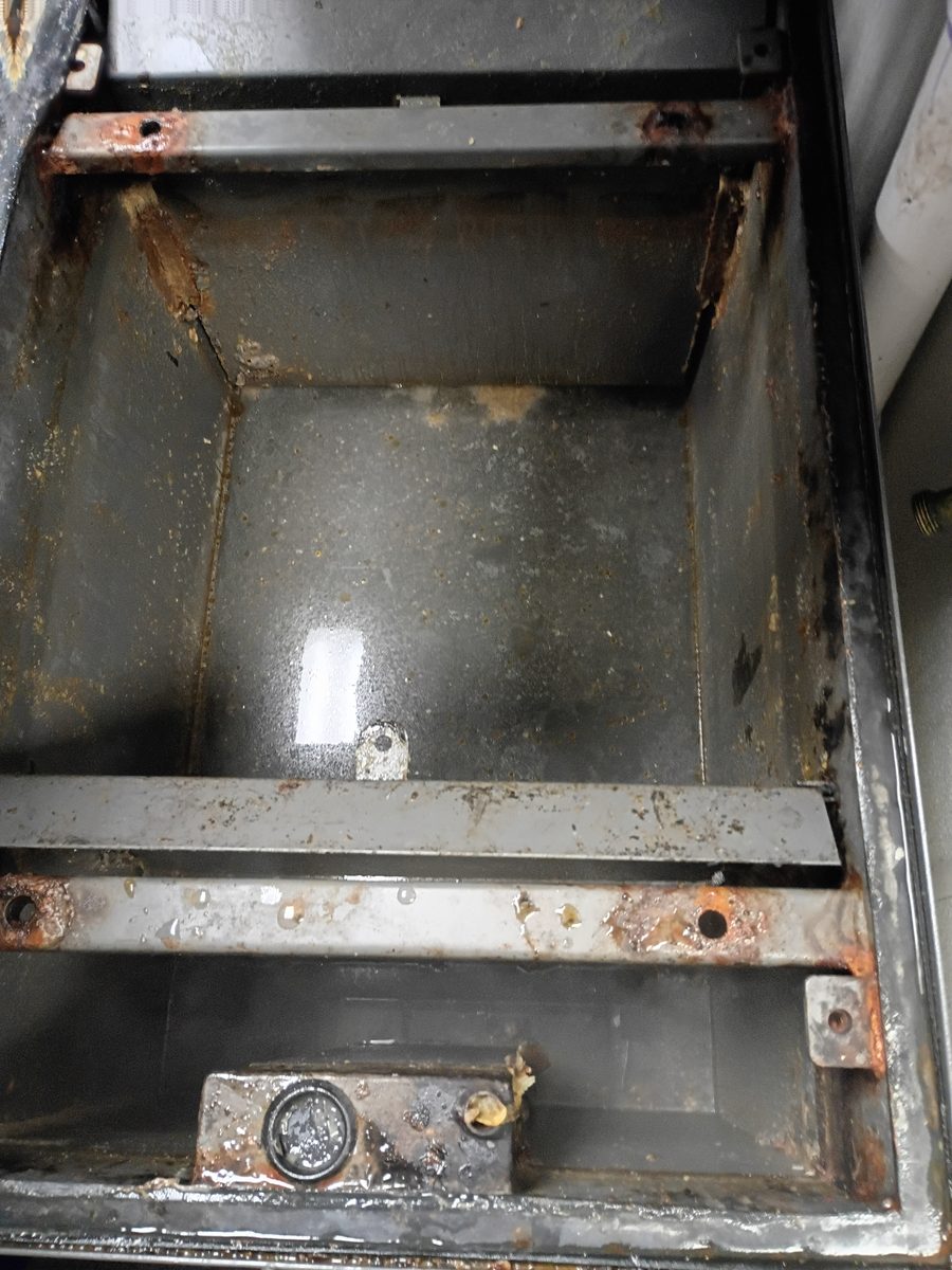 After grease trap cleaning, the same indoor grease trap compartment is pumped down with the metal basin visible and floating grease removed.