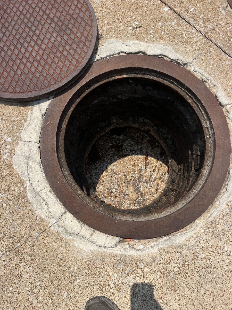 Before outdoor grease trap cleaning, an open manhole-style grease trap access shows a thick layer of grease and solids inside.